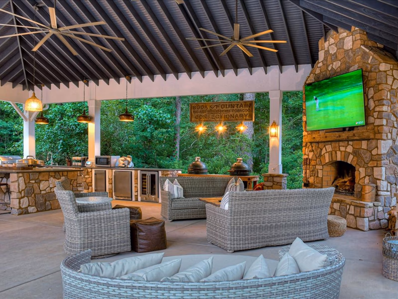 An open-air, covered patio with a TV screen, outdoor kitchen, and fans on the ceiling.