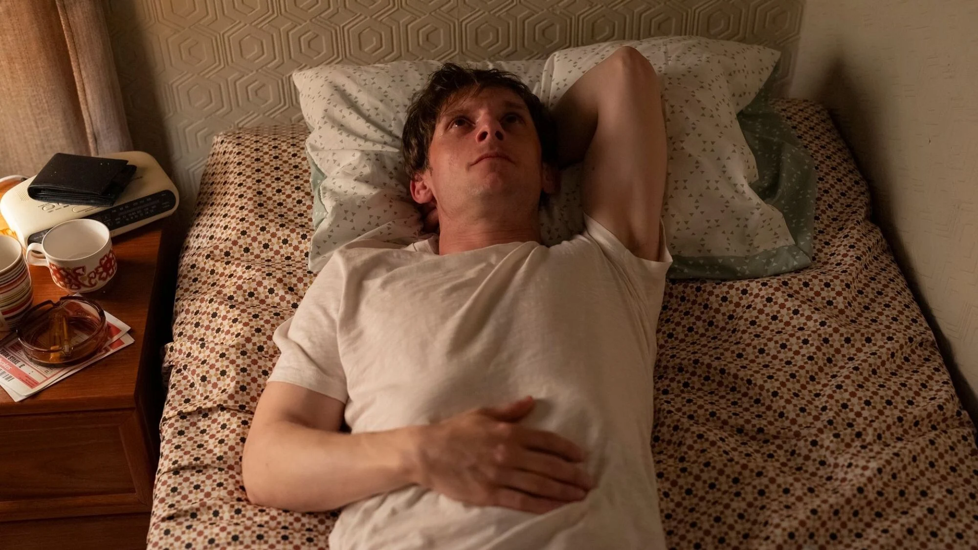 A young man lies on a bed looking up at the ceiling.