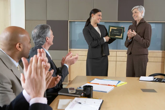 Executives applauding for woman holding "Employee of the Month" plaque