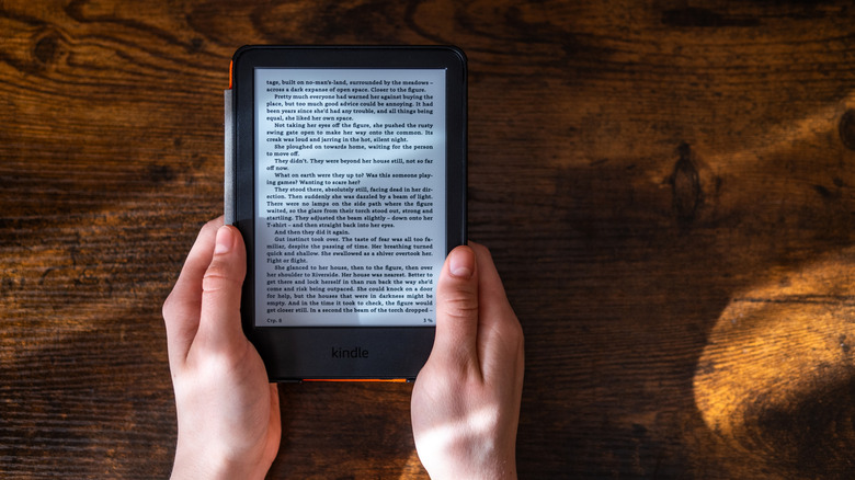 Hands holding an Amazon Kindle against a wood backdrop