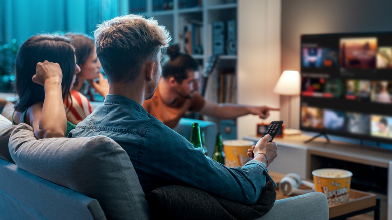 A person holding a remote to navigate a smart T.V.'s interface, while other people look on