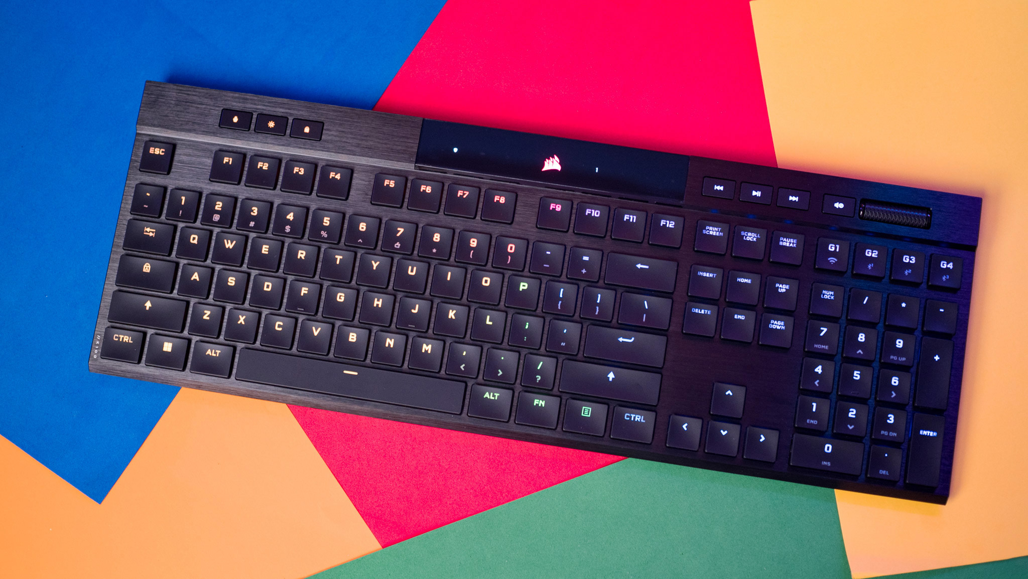 A sleek black mechanical keyboard with backlit keys is angled on a colorful geometric background of blue, red, orange, and green, conveying a modern, vibrant feel.