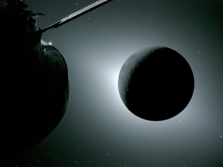 At left, part of a spacecraft. At right, the moon looking like a levitating black ball in front of a bright light source.