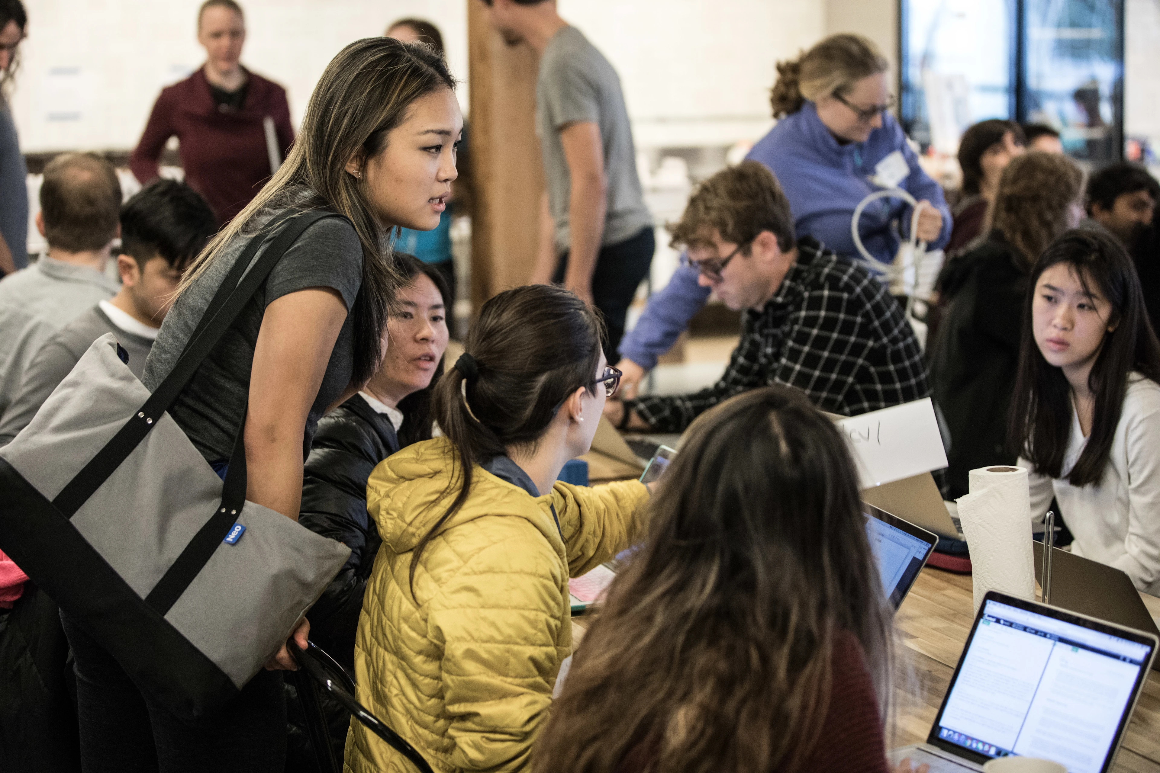 Person looking over the shoulder of people sitting around a table with laptops