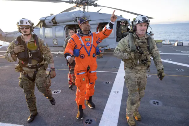 Victor Glover, piloto de Artemis II, es asistido para bajar de la cubierta de vuelo tras llegar a bordo del USS John P. Murtha. Junto con sus compañeros de tripulación.