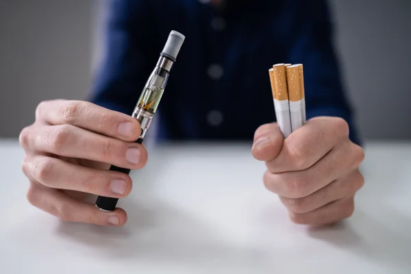 A man holds cigarettes and vapes