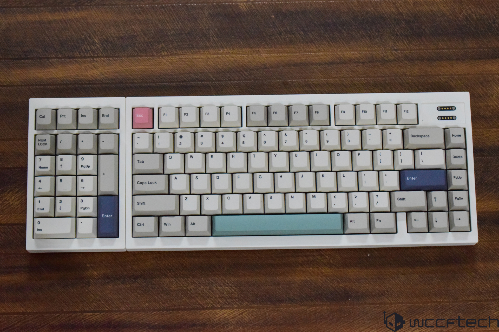 A mechanical keyboard with a pink 'Esc' key and a mint green space bar, featuring white and gray keycaps on a wooden surface.