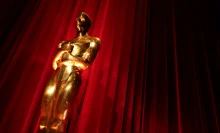 A shiny Oscar statue in front of a red curtain.