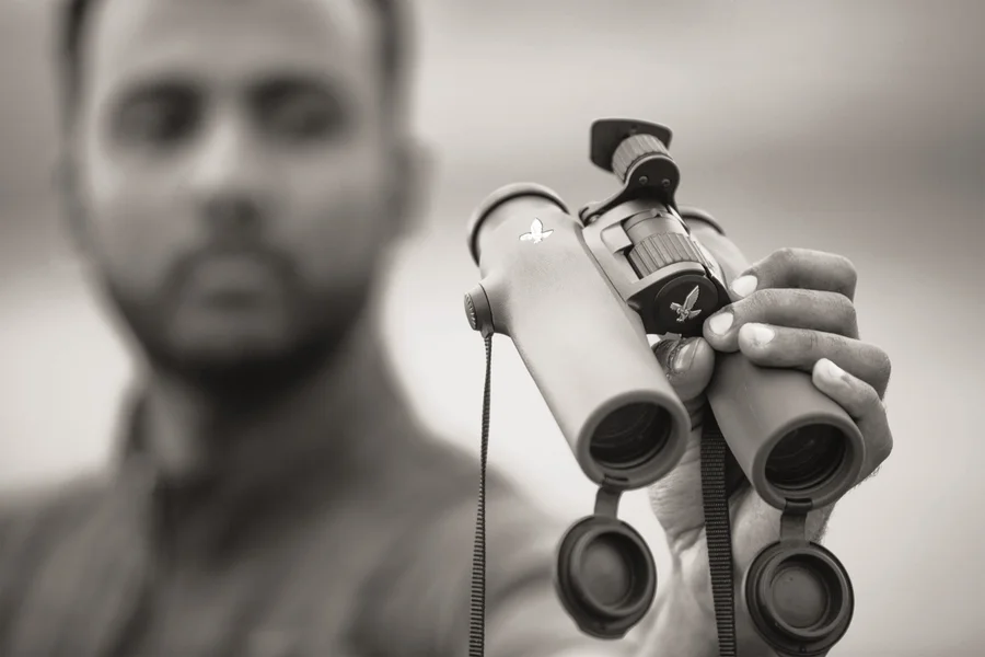 A black and white photo of a man holding a pair of binoculars, with the man blurred in the background.
