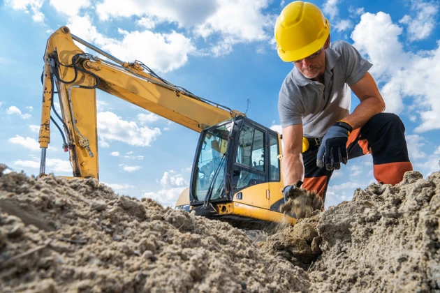 Construction Worker Digging a Trench With Excavator on Sunny Day in the City