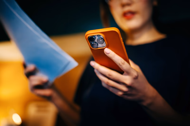 Close-up shot of young Asian woman using her smartphone for scanning the QR code and paying bills from home with e-banking app. Financial technology. Internet banking. Home finances. Managing personal banking and finance at easy access