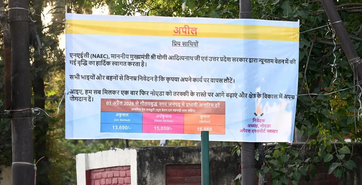 A banner installed by the Noida Apparel Export Cluster (NAEC) in Nagla Charan Dass, Phase-2, Noida, on April 15, 2026, notes the revised wages. It reads: “The NAEC welcomes the increase in minimum wage by Chief Minister Adityanath and the government of Uttar Pradesh. We humbly request all brothers and sisters to return to work. Let us once again take Noida forward on the path of progress and contribute to the development of the region.”