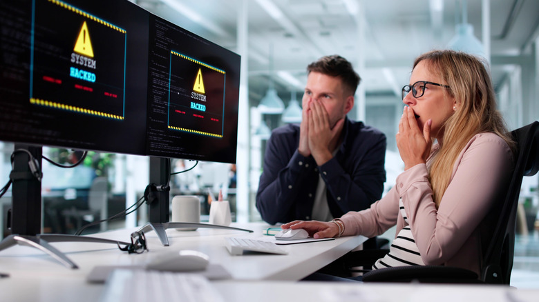 Office computers displaying "system hacked" message with people reacting.
