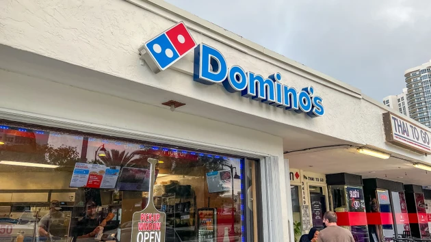 Domino"s Pizza storefront with blue and red signage, open for business, featuring a visible menu display and customers outside in a commercial area