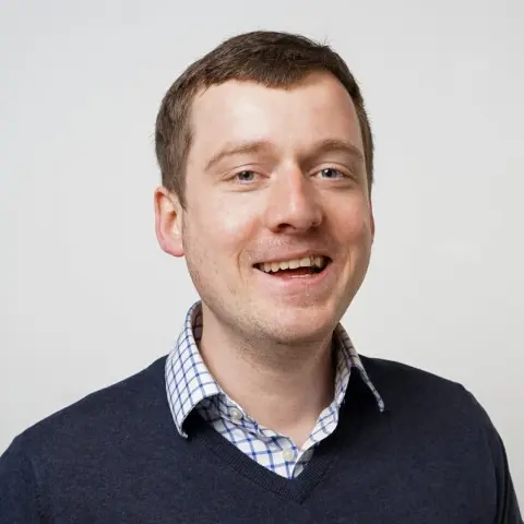 A smiling man with short… shirt under his jumper