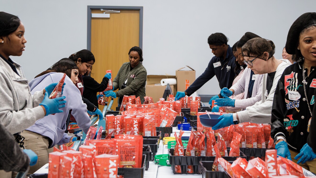 Volunteers packing food items in red bags for community service