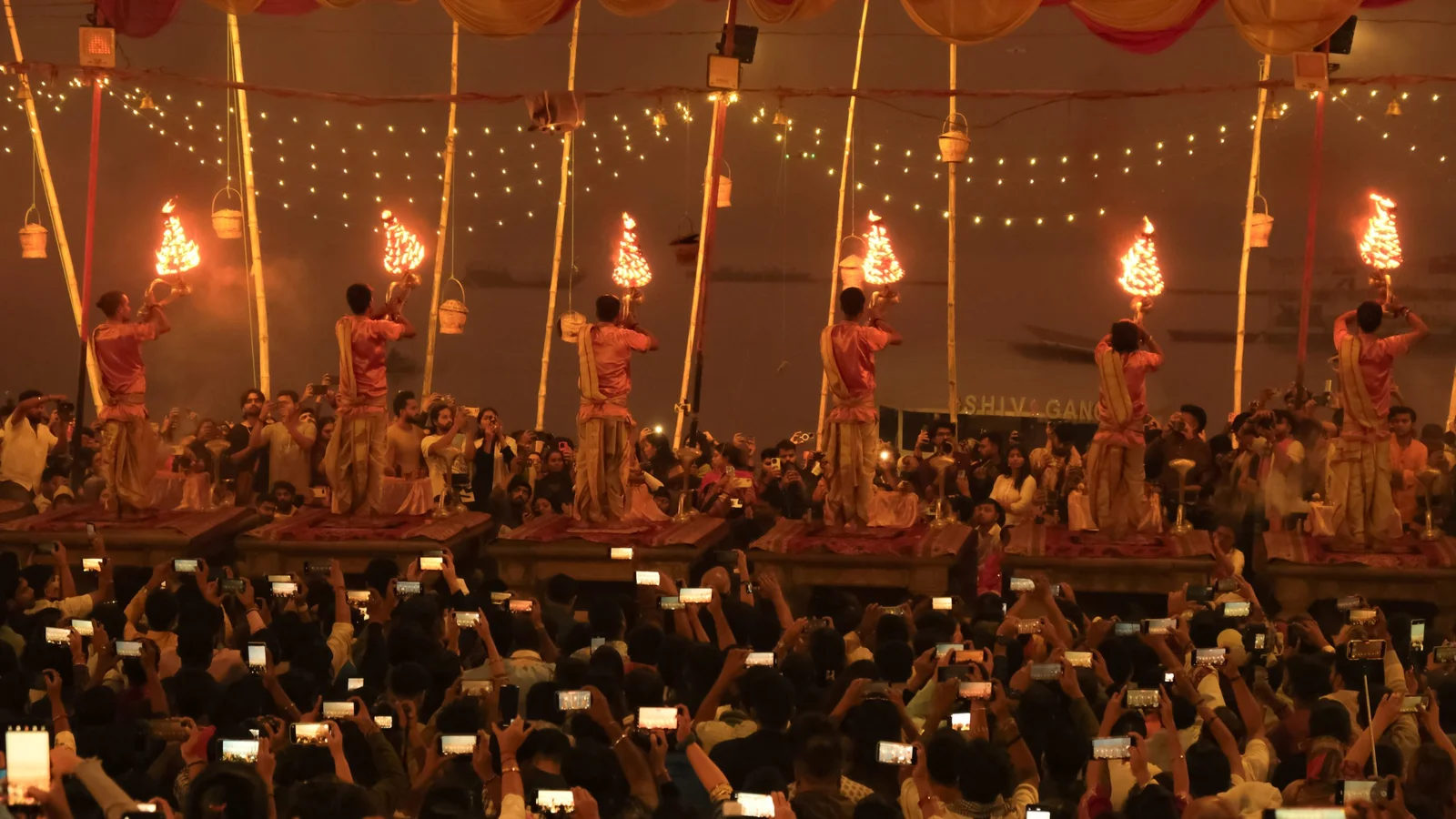 A crowd watches as performers conduct a ritual with flaming torches on elevated platforms during a festive event.