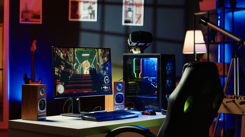 Gaming PC setup with monitor, RGB case, speakers, and VR headset on a desk.