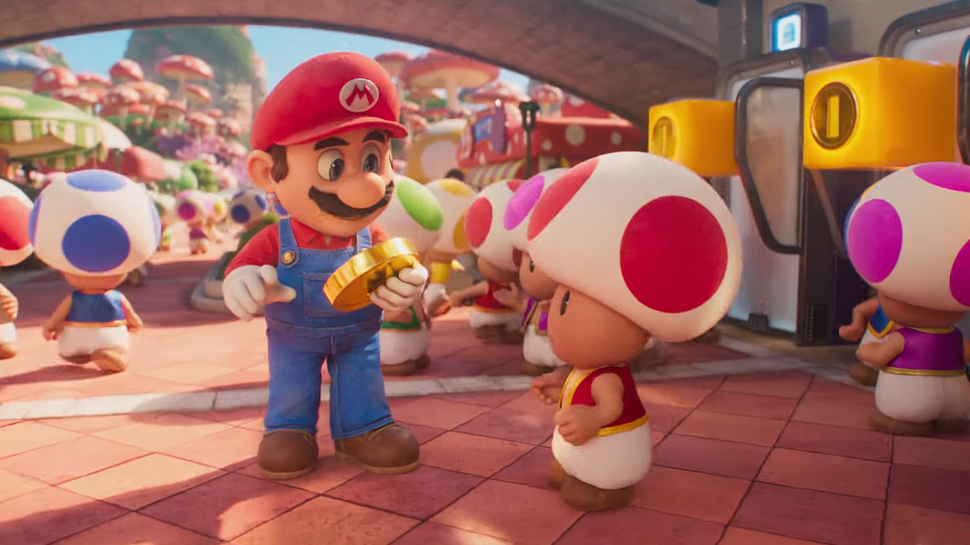 Mario from the Nintendo franchise holds a large coin while surrounded by Toad characters in a vibrant, mushroom-filled environment.