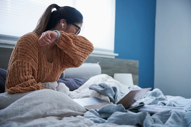 Woman coughing into elbow while sitting in bed