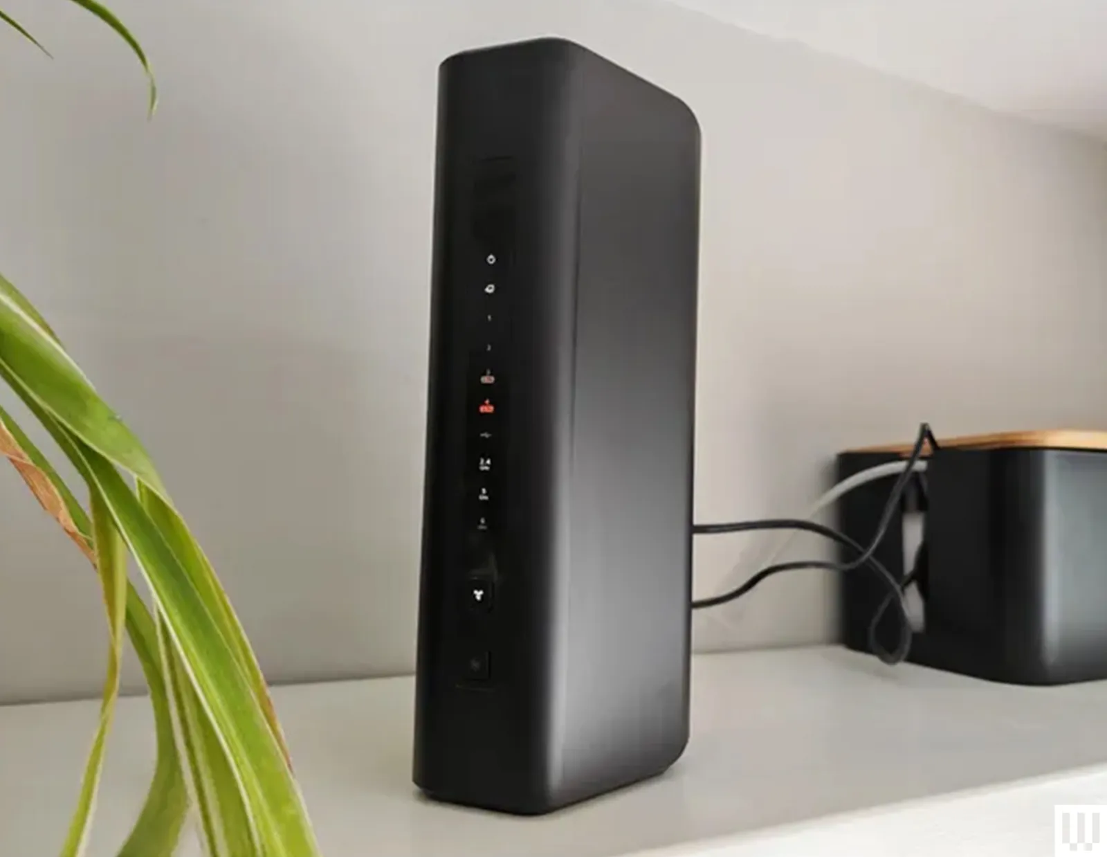 Netgear Nighthawk RS300 wifi router a black narrow device sitting on a white shelf with 2 wires coming from the back