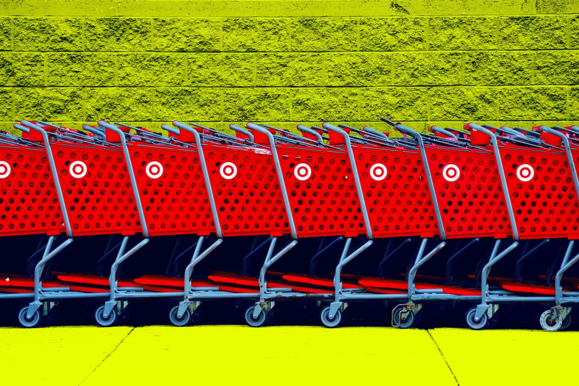 A row of red Target shopping carts lined up side by side against a textured yellow brick wall and yellow ground. The carts have the distinctive white Target logo on their sides.