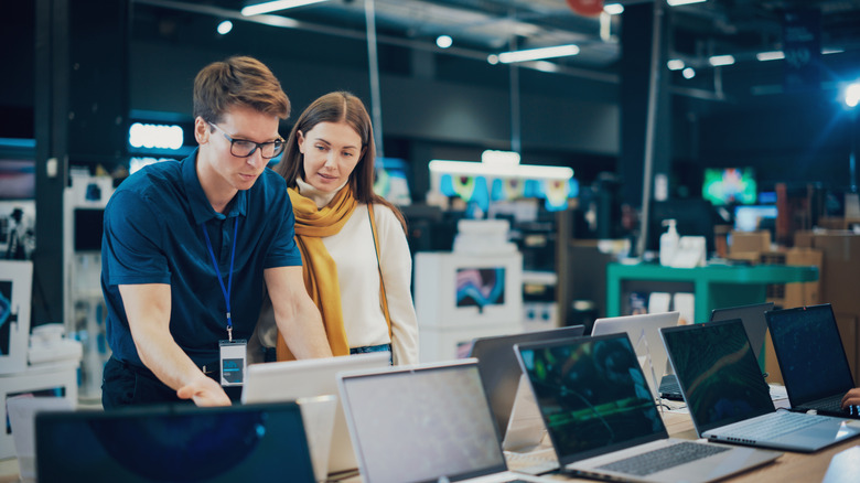 A woman shopping for laptops while a store associate demonstrates features on one model.