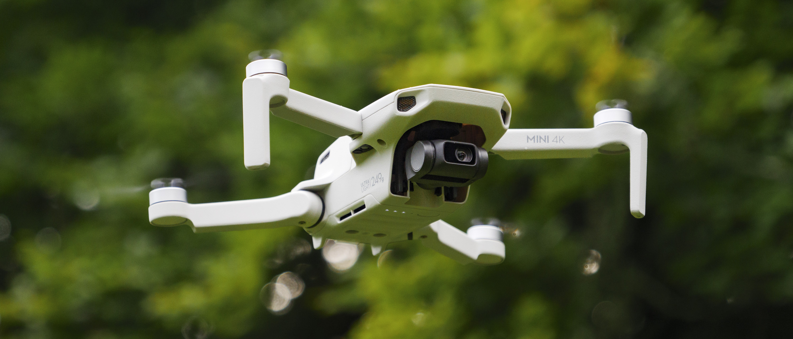 DJI Mini 4K beginner drone in flight with soft focus tree foliage in the background