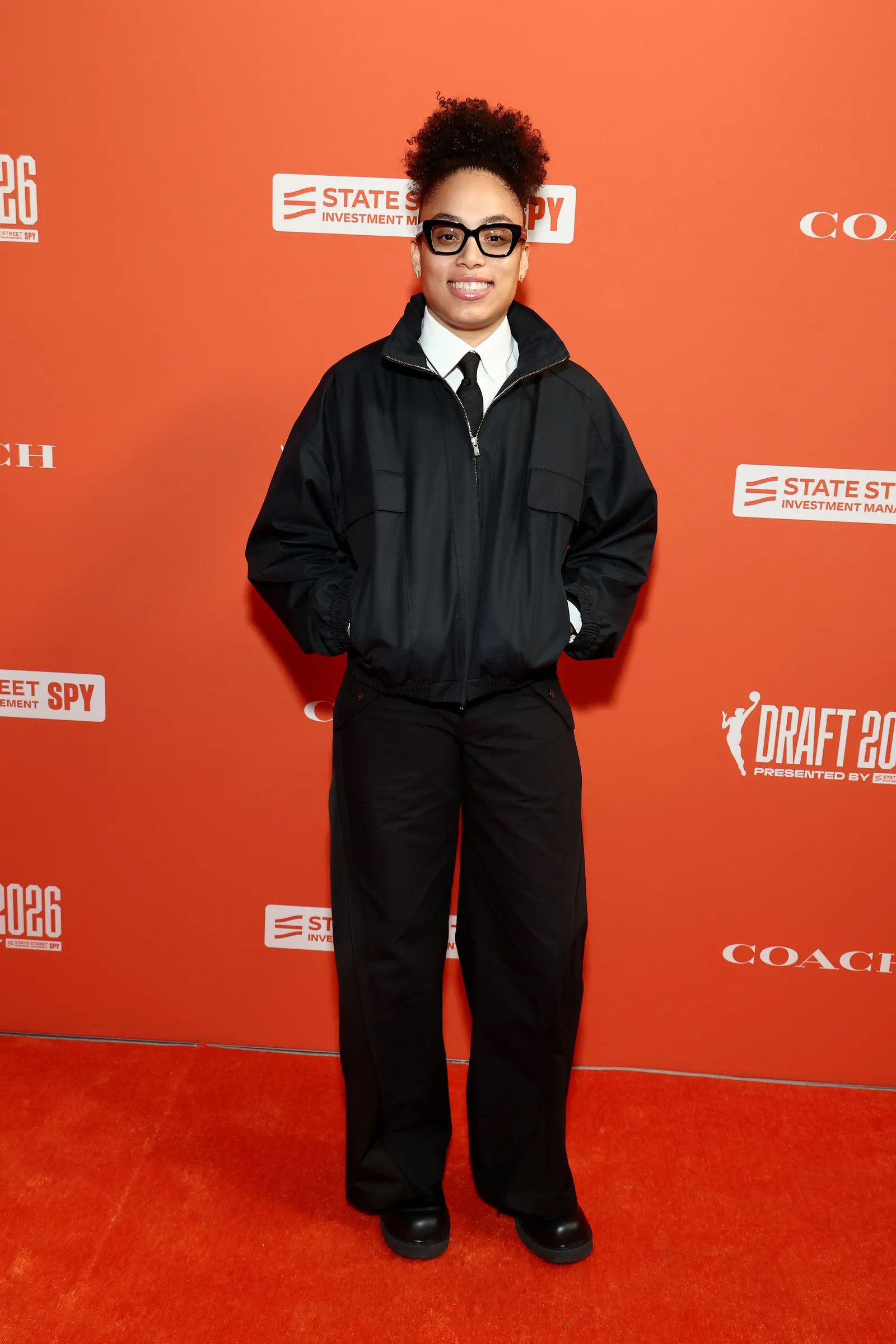 Image may contain Fashion Adult Person Clothing Coat Jacket Accessories Glasses Formal Wear Suit and Standing