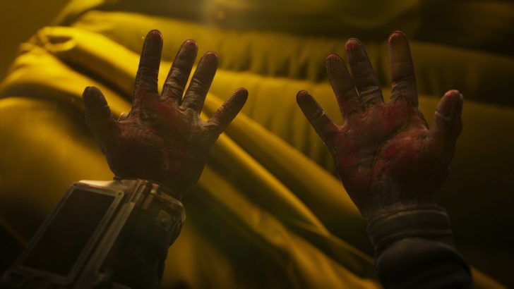 Gloved hands reaching towards a yellow fabric in a dimly lit environment.