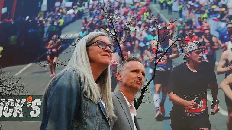 Denise and Bill Richard walk past a mural photo of Boston Marathon runners hanging on a building on Boylston Street.