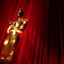 A shiny Oscar statue in front of a red curtain.