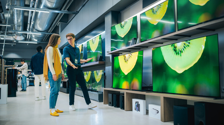 A person speaking with a sales associate while shopping for TVs