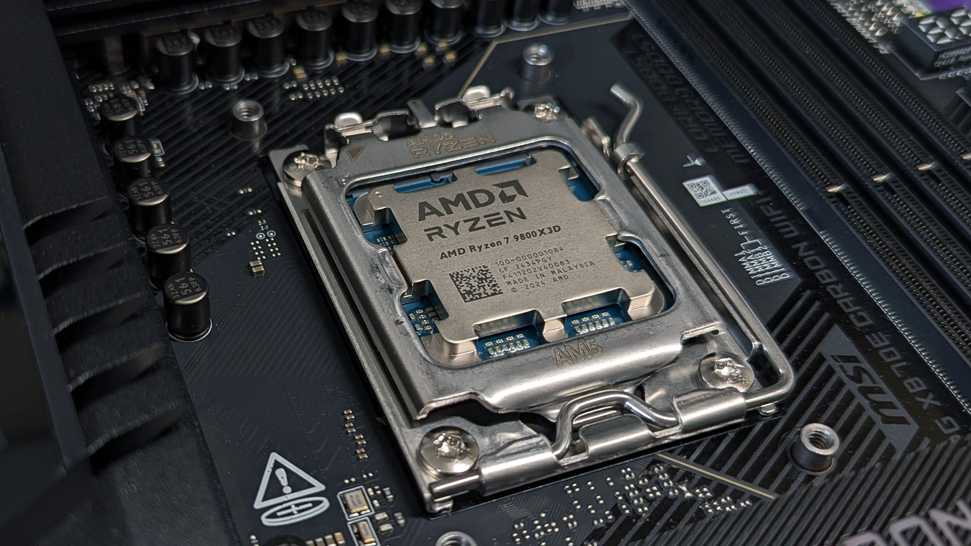 Close-up of an AMD Ryzen 7 9800X3D CPU installed on a motherboard. The metallic processor is securely placed, with surrounding circuitry visible.