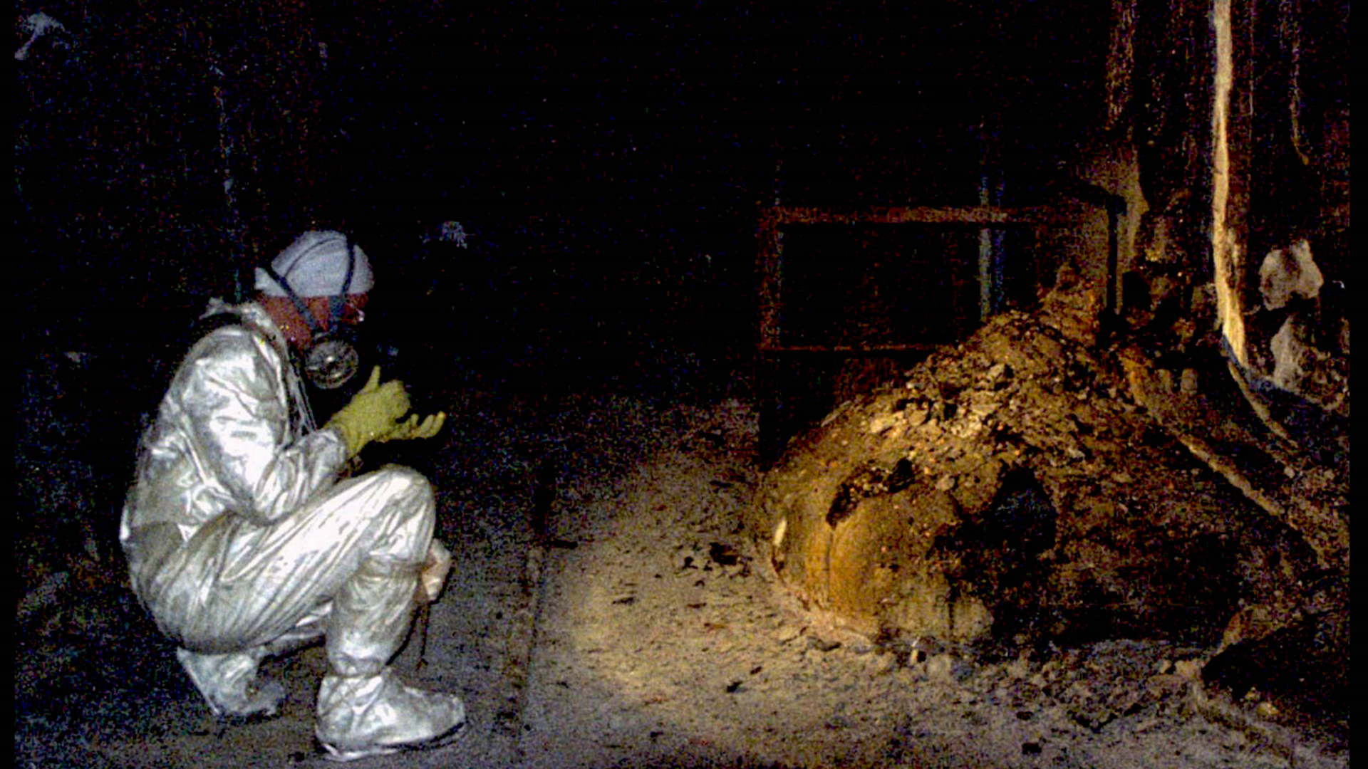A person wearing a shiny hazmat suit takes a photo of a pile of debris in the middle of the Chernobyl power plant.