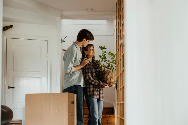 Man kissing girlfriend holding plant while standing in new home