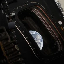 One half of the Earth is seen floating in space through the open door of the Orion spacecraft.