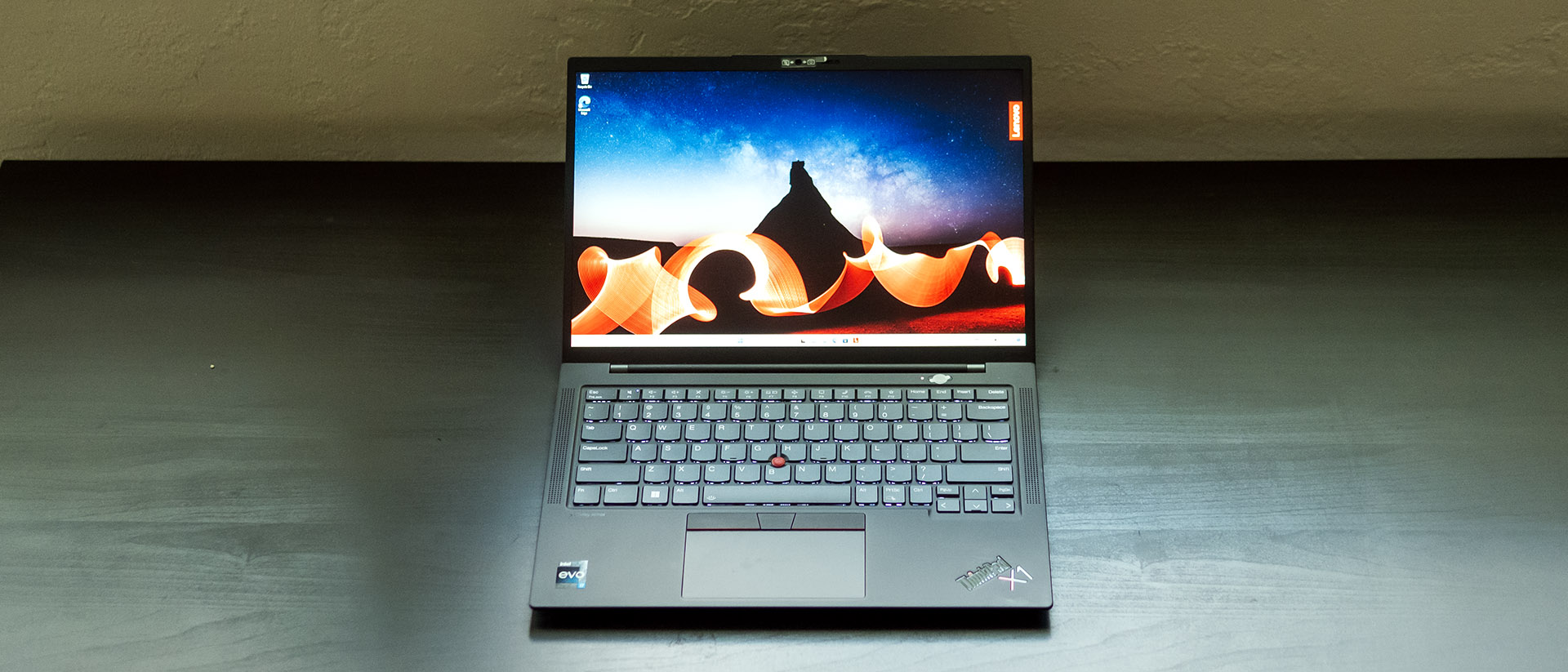 The Lenovo ThinkPad X1 Carbon on a black background. The familiar design, including a red Trackpoint, showcases its focus on reliability for work.