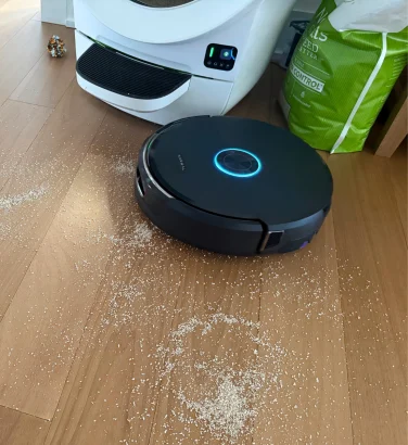 Narwal Flow 2 robot vacuum cleaning cat litter on hardwood floor near litter box