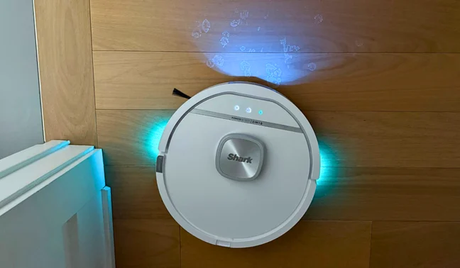 Shark PowerDetect UV Reveal 2-in-1 robot vacuum illuminating dried stain on hardwood floor