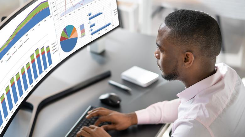 A man works at a curved monitor with graphs on the screen
