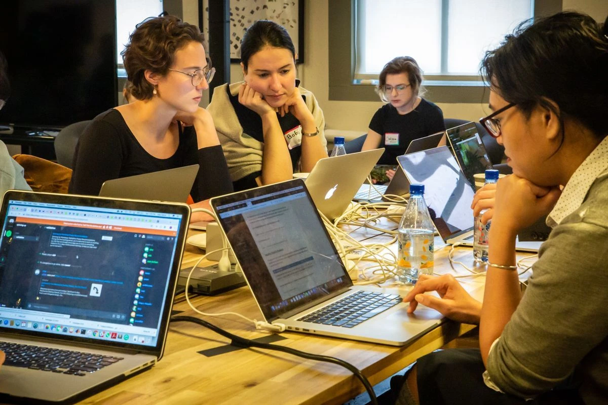 Group of people sitting together around a table, focused on their laptops