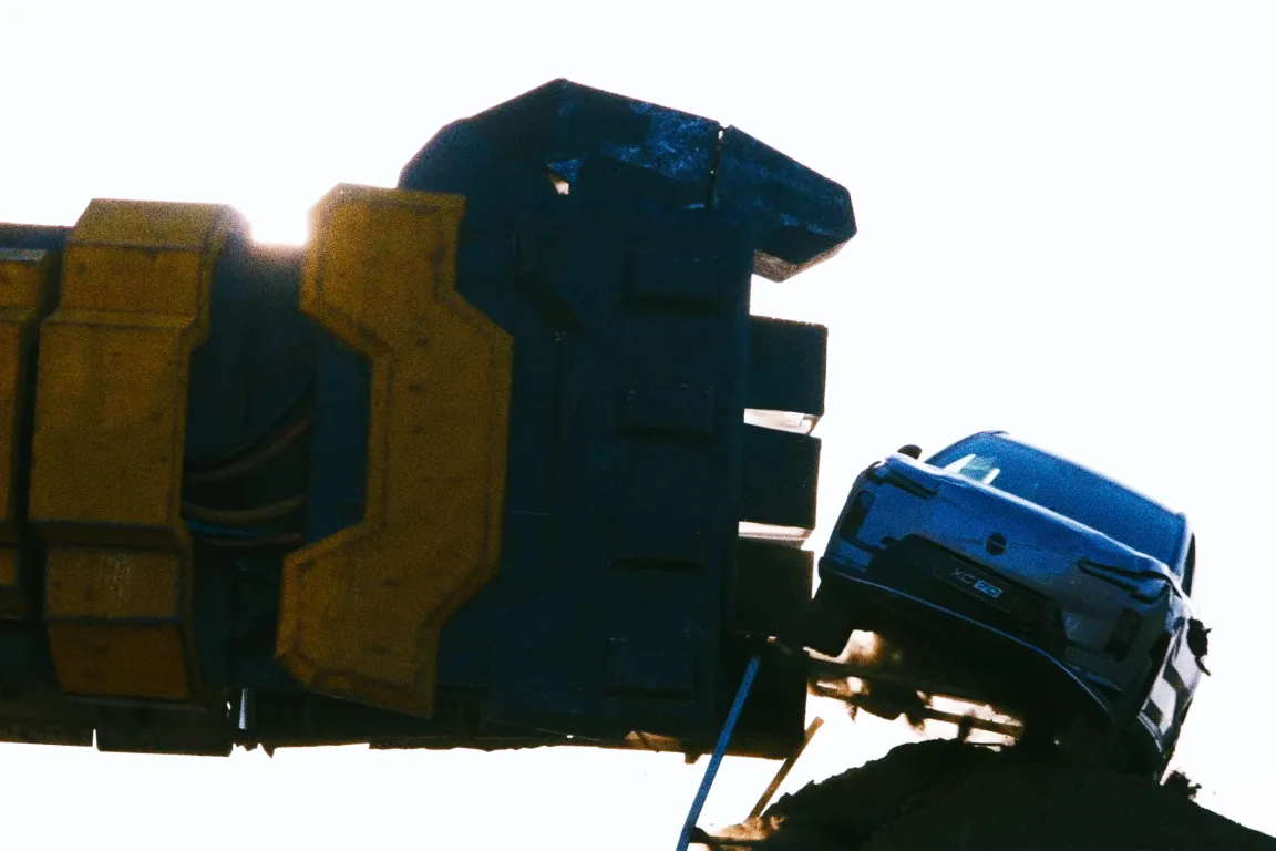 A blue Volvo XC90 SUV is being punched by a gigantic robot arm.
