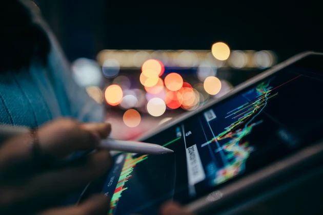 Close-up of female hands holding a mobile phone, browsing the stock market charts on a city street at night, with blurred car and street lights in the background