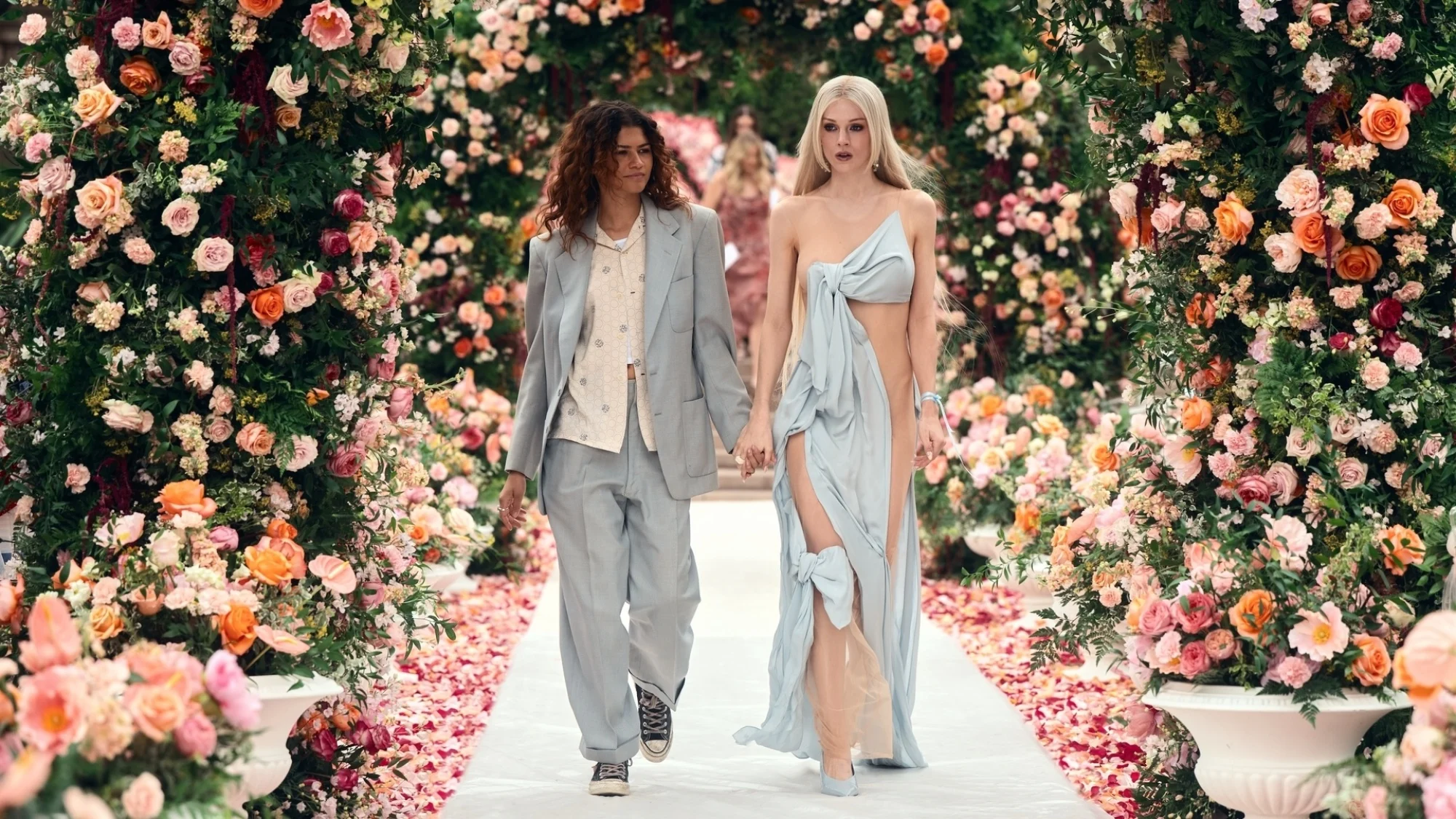 Two characters walk down a rose-flanked aisle.