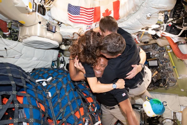 Surrounded by equipment, the crew of the Artemis II mission embraces in microgravity in the center of the frame