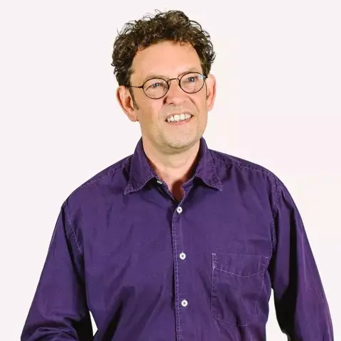 A smiling man with curly…wearing a purple shirt.