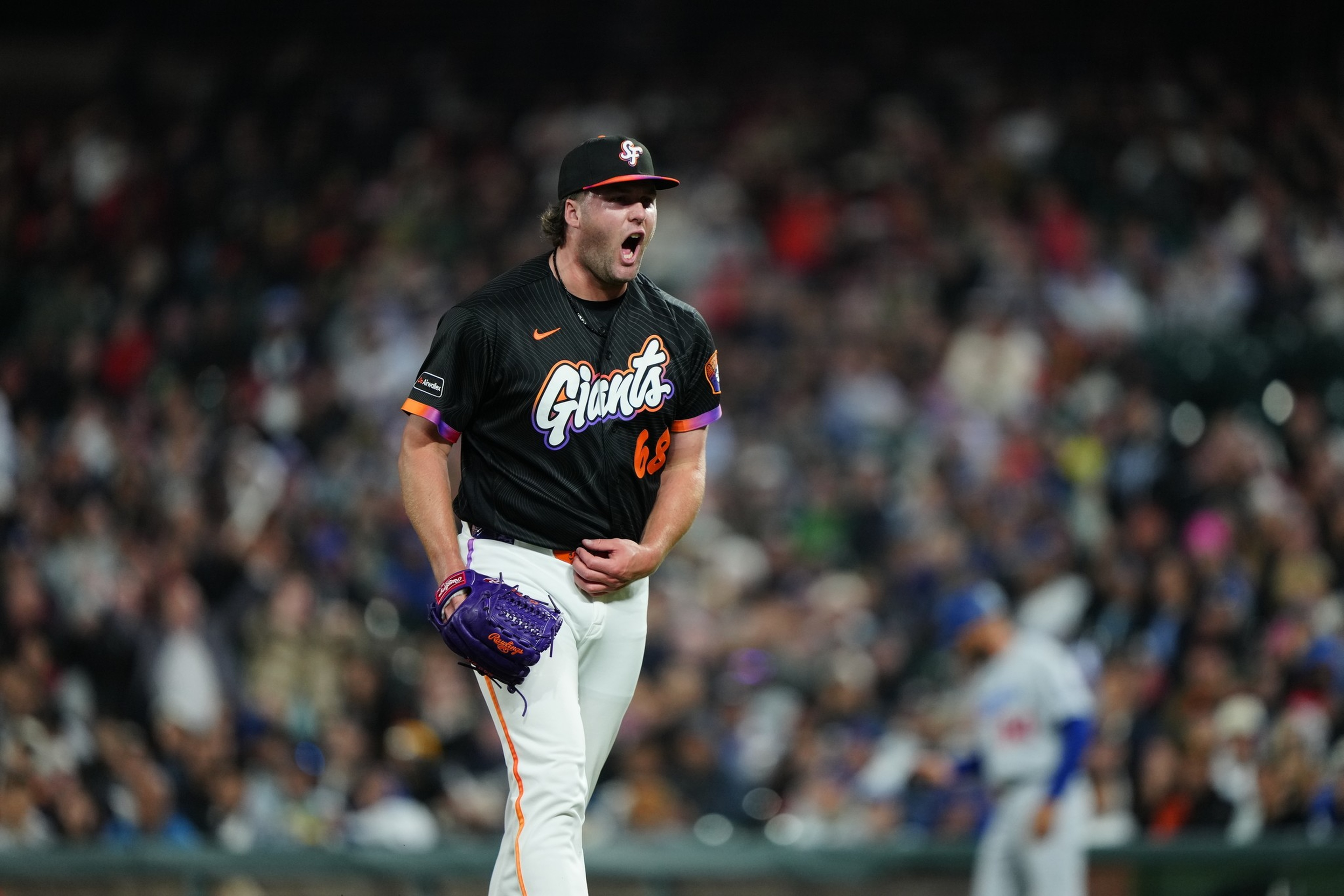 A San Francisco Giants pitcher celebrates with a yell on the mound during a night game in front of a blurred crowd.