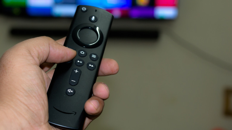 A person points a black Amazon First Stick report towards a TV home screen.