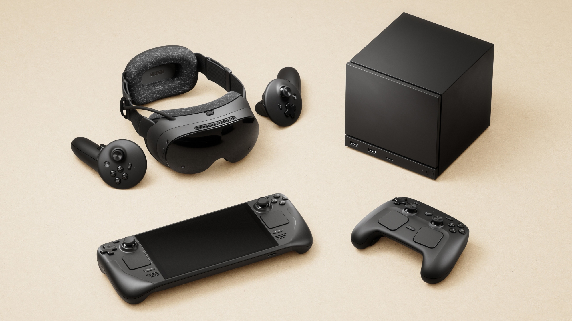 A set of black gaming devices on a tan surface, including the Steam Frame VR headset, Steam Controller, Steam Deck handheld console, and the cube-shaped Steam Machine, all sleek and modern.